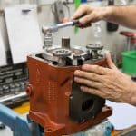 Hände eines Mitarbeiters von Motrac Hydraulic, der eine Hydraulik-Einheit wartet bzw. repariert.